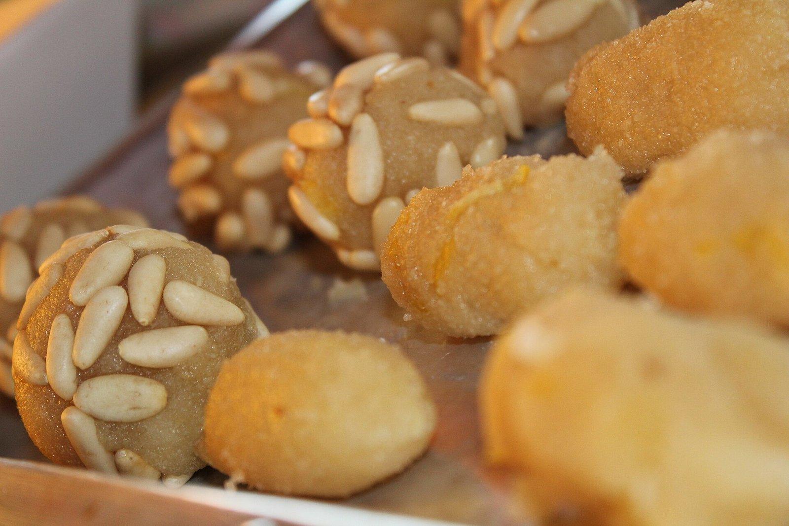 Primer plano de panellets, dulces tradicionales, unos cubiertos de piñones y otros alargados, sobre una bandeja metálica