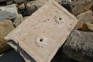 Losa de mármol con dos rosetas talladas con un orificio, entre bloques de piedra, detalle del anfiteatro de Tarragona.