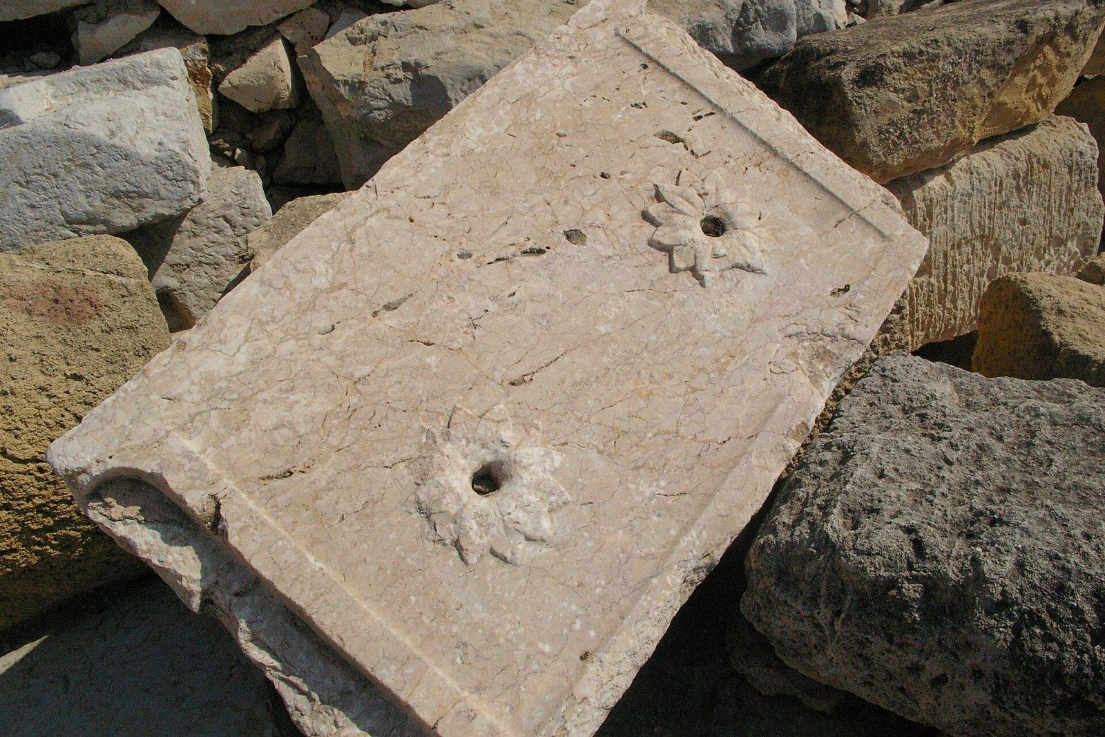 Losa de mármol con dos rosetas talladas con un orificio, entre bloques de piedra, detalle del anfiteatro de Tarragona.