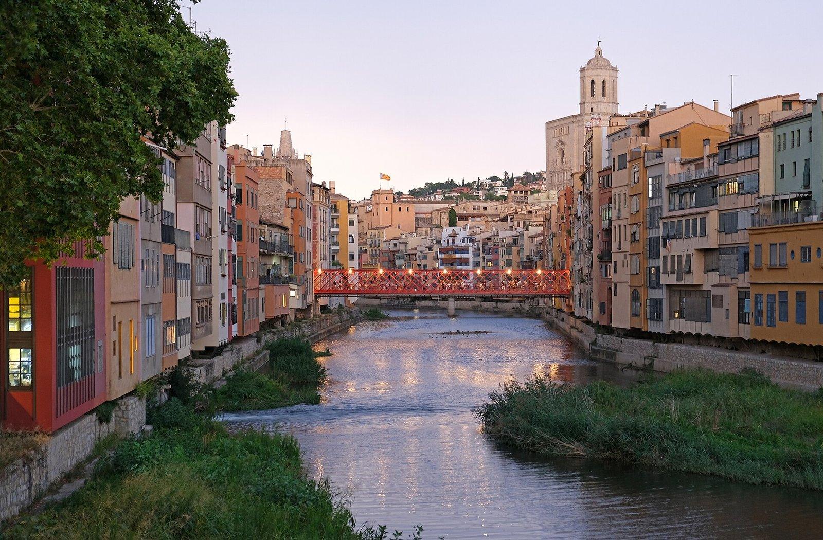 Casas de colores junto al río Onyar al atardecer, con el puente rojo de las Peixateries Velles y la Catedral al fondo.